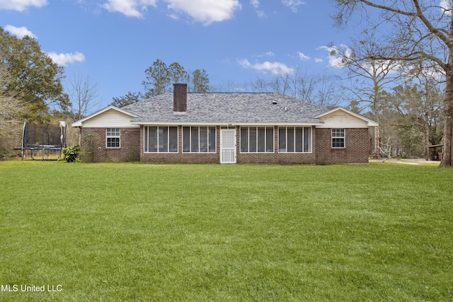 rear view of house featuring a sunroom, a chimney, a trampoline, a yard, and brick siding