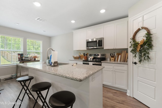 14172 Debra Barbee Ct, Gulfport, MS 39503 - kitchen with stainless steel appliances, an island with sink, light wood-type flooring, white cabinets, and a breakfast bar area