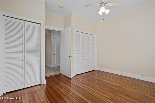 unfurnished bedroom featuring wood-type flooring, baseboards, and multiple closets