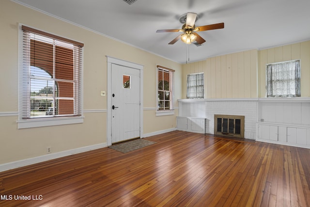 unfurnished living room with ceiling fan, hardwood / wood-style flooring, baseboards, ornamental molding, and a brick fireplace