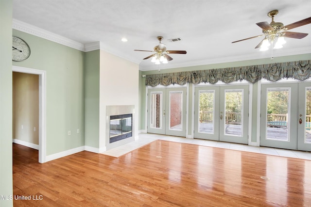 unfurnished living room featuring a fireplace, crown molding, light hardwood / wood-style flooring, and french doors