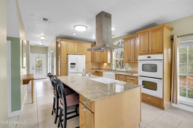 kitchen with plenty of natural light, island range hood, white appliances, and an island with sink