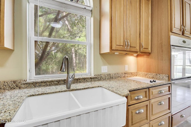 kitchen with white double oven, light stone counters, and sink