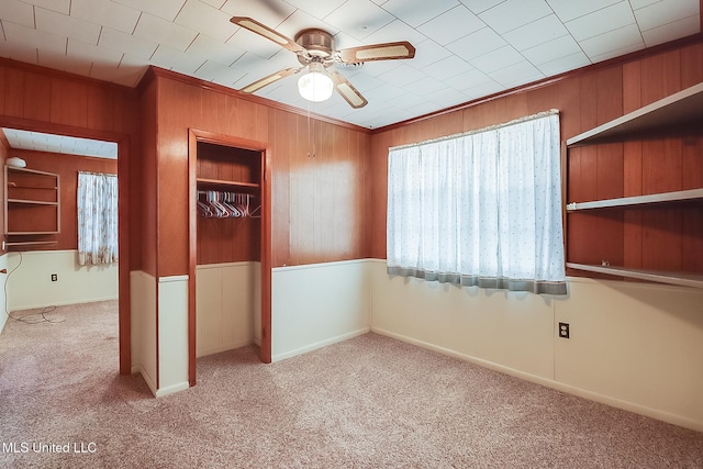 carpeted empty room featuring ceiling fan, ornamental molding, and wood walls