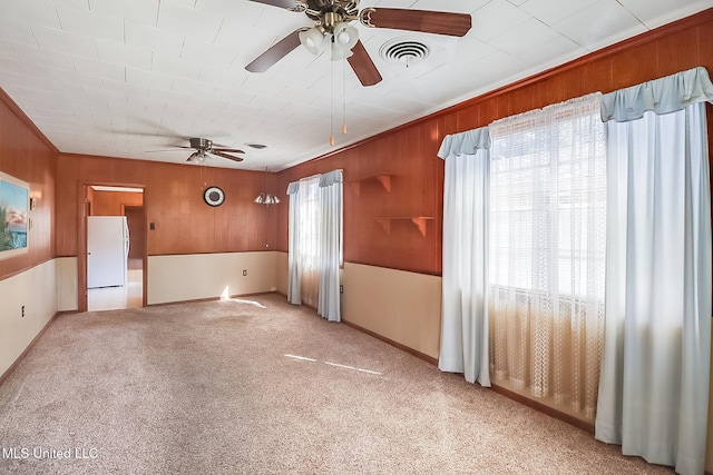 carpeted spare room featuring ornamental molding, ceiling fan, and wooden walls