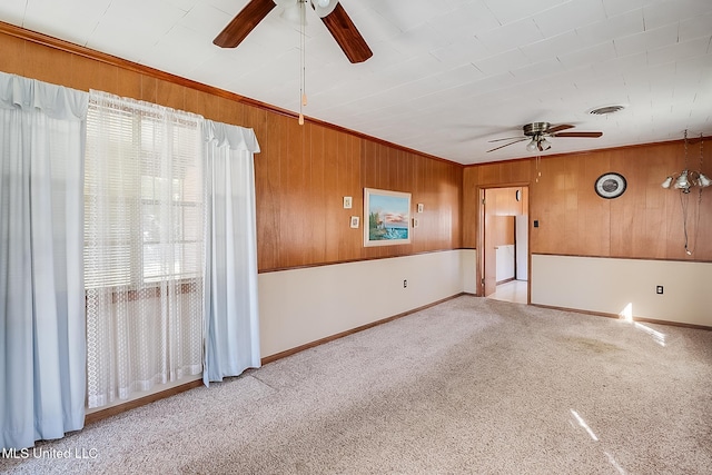 empty room with ceiling fan, wood walls, crown molding, and light carpet