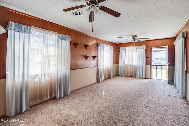 unfurnished room featuring ceiling fan, a healthy amount of sunlight, and wood walls