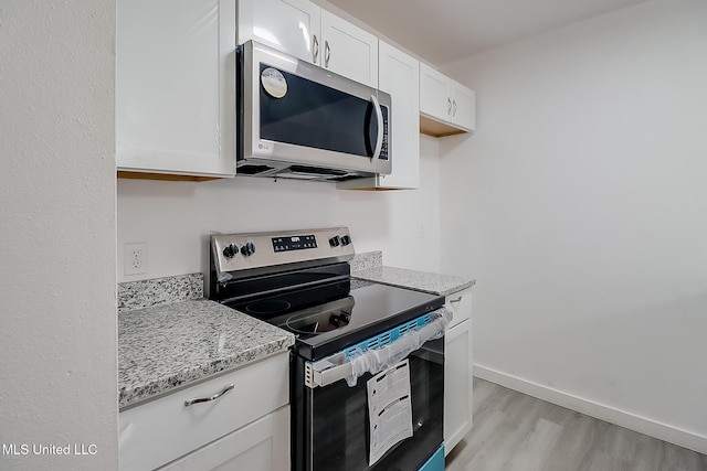 kitchen featuring light stone counters, light wood finished floors, stainless steel appliances, white cabinets, and baseboards