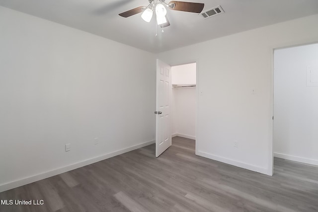 unfurnished bedroom with visible vents, a spacious closet, baseboards, and wood finished floors