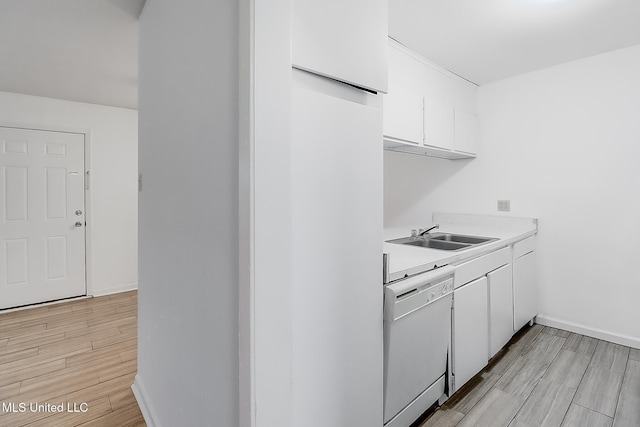 kitchen featuring white dishwasher, a sink, white cabinets, light countertops, and light wood-type flooring