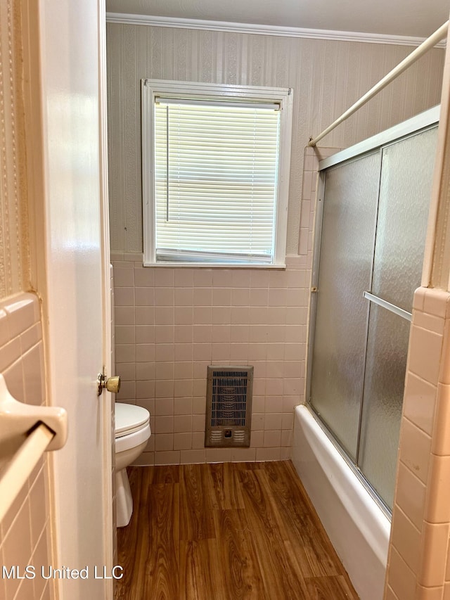 176 Revell Rd, Grenada, MS 38901 - bathroom featuring heating unit, wood finished floors, toilet, shower / bath combination with glass door, and tile walls