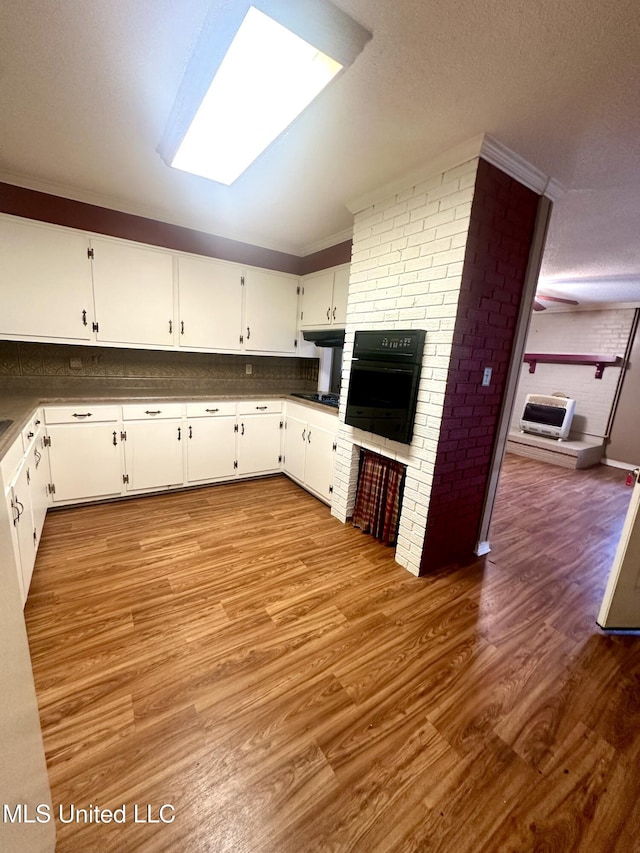 176 Revell Rd, Grenada, MS 38901 - kitchen featuring black appliances, a brick fireplace, wood finished floors, white cabinets, and a textured ceiling