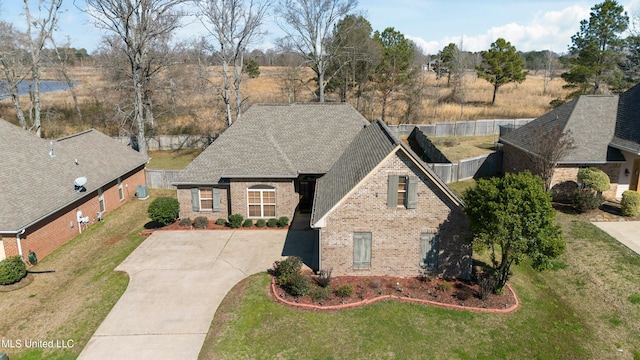 view of front of house featuring brick siding, roof with shingles, concrete driveway, a front yard, and fence