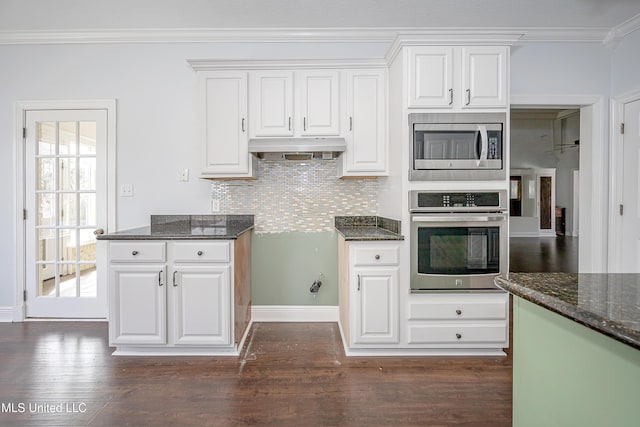 kitchen featuring under cabinet range hood, white cabinetry, appliances with stainless steel finishes, ornamental molding, and dark stone counters