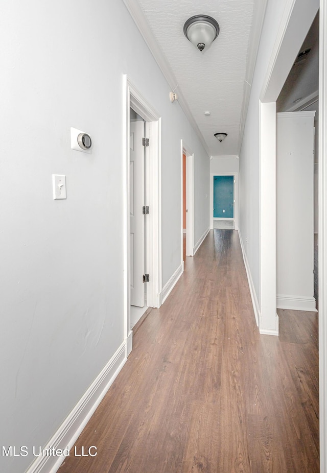 corridor with baseboards, wood finished floors, and ornamental molding