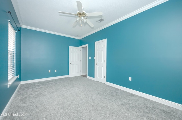 spare room with baseboards, visible vents, a ceiling fan, ornamental molding, and carpet flooring