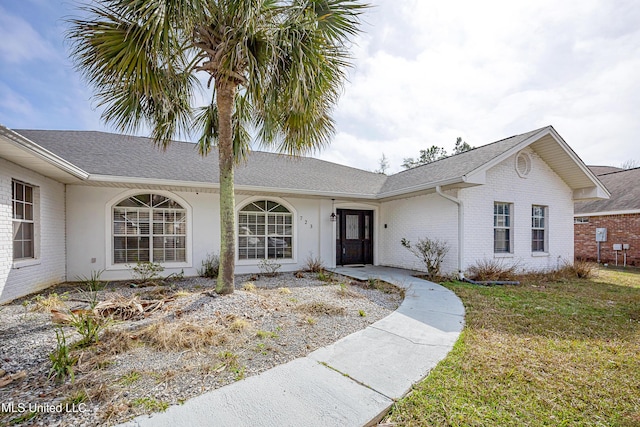 single story home featuring roof with shingles, a front lawn, and brick siding