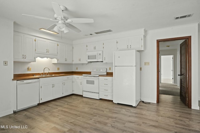 kitchen with white appliances, wood finished floors, a sink, visible vents, and dark countertops