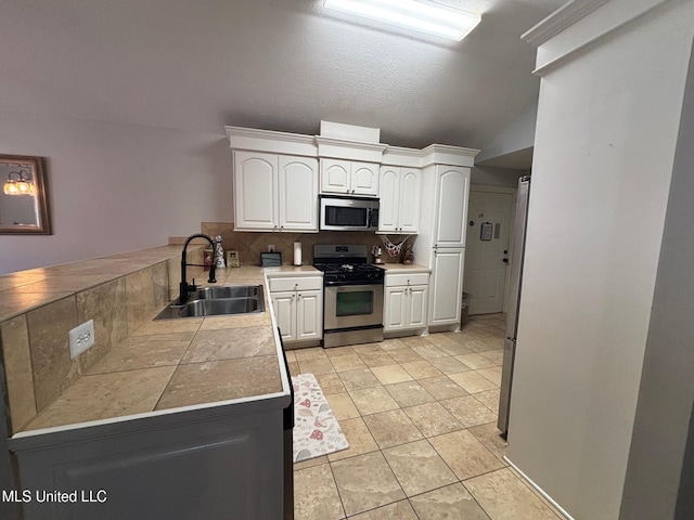 kitchen with backsplash, sink, vaulted ceiling, white cabinetry, and stainless steel appliances