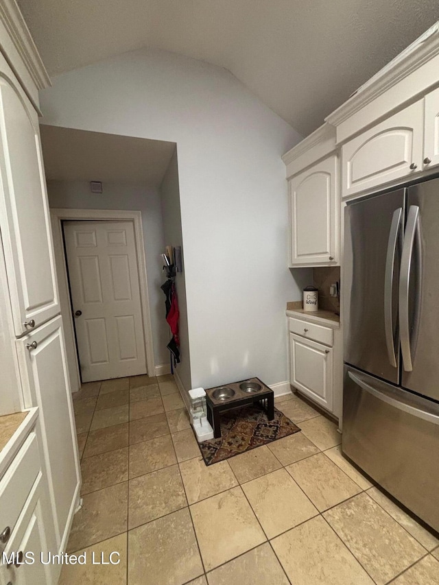 kitchen featuring light tile patterned floors, white cabinetry, stainless steel refrigerator, and vaulted ceiling