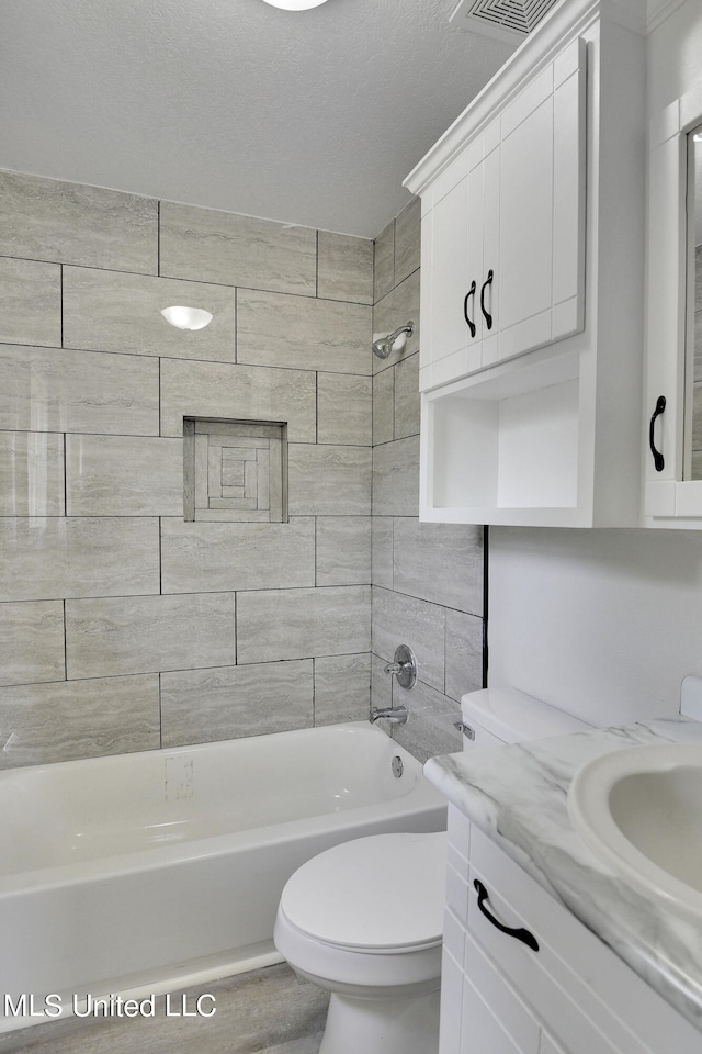 full bathroom featuring tiled shower / bath, a textured ceiling, hardwood / wood-style flooring, toilet, and vanity