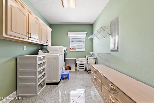 washroom with electric panel, washing machine and dryer, a textured ceiling, and cabinets