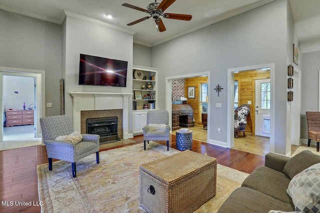 living room featuring ceiling fan, ornamental molding, a towering ceiling, and light wood-type flooring