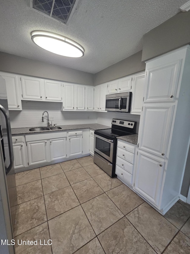 1442 Tally Ho Cir, Gulfport, MS 39507 - kitchen with appliances with stainless steel finishes, a textured ceiling, white cabinetry, and light tile patterned floors
