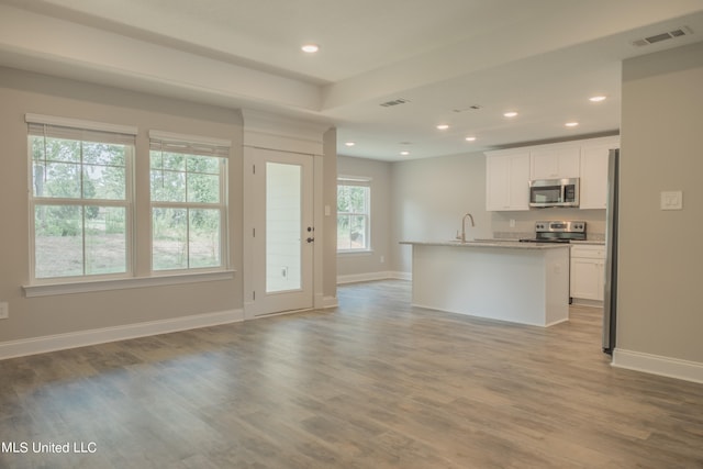 kitchen with a wealth of natural light, appliances with stainless steel finishes, a kitchen island with sink, and white cabinets