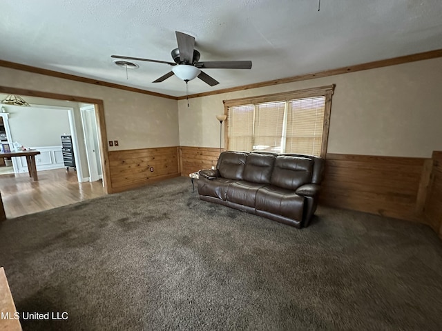 living room featuring a ceiling fan, crown molding, carpet floors, a wainscoted wall, and wood walls