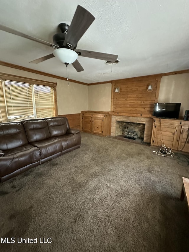 living area featuring carpet flooring, wood walls, ceiling fan, crown molding, and a fireplace