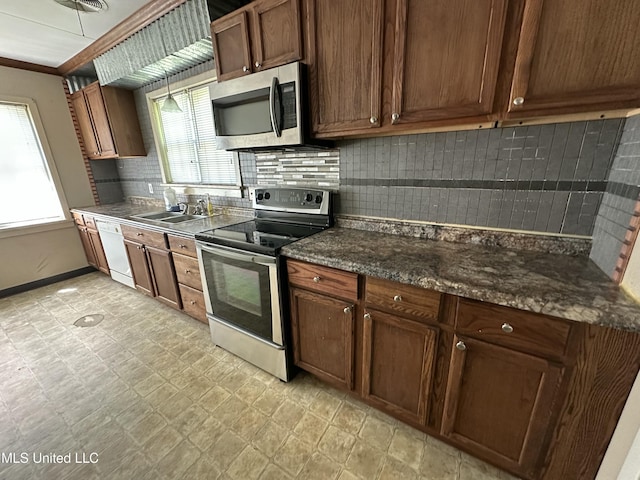 kitchen with dark countertops, a sink, decorative backsplash, baseboards, and appliances with stainless steel finishes