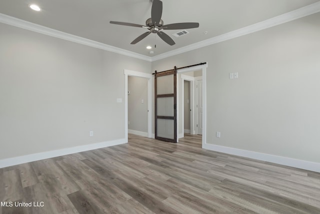 unfurnished bedroom featuring light hardwood / wood-style floors, ornamental molding, a barn door, and ceiling fan