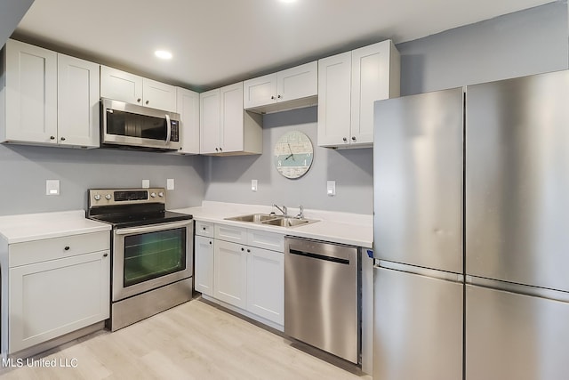 kitchen with sink, appliances with stainless steel finishes, light hardwood / wood-style flooring, and white cabinets