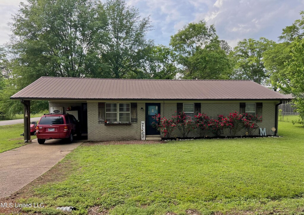ranch-style home with a front lawn, driveway, metal roof, a carport, and brick siding
