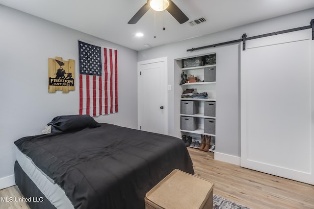 8707 Pine Ridge Ct, Diamondhead, MS 39525 - bedroom featuring a barn door, light wood-style flooring, and ceiling fan