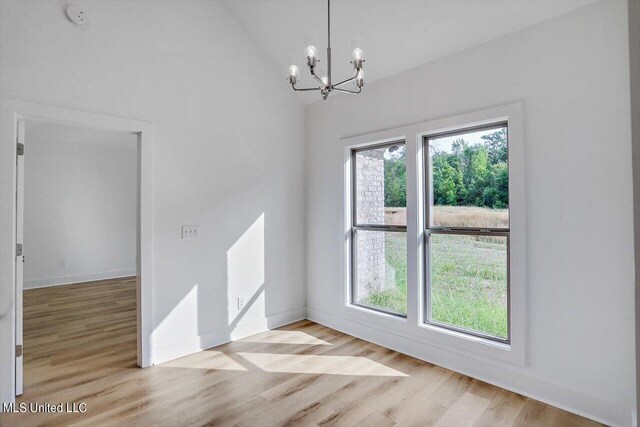 empty room with vaulted ceiling, an inviting chandelier, and light hardwood / wood-style floors