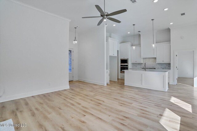 unfurnished living room with ceiling fan, sink, a high ceiling, crown molding, and light hardwood / wood-style flooring