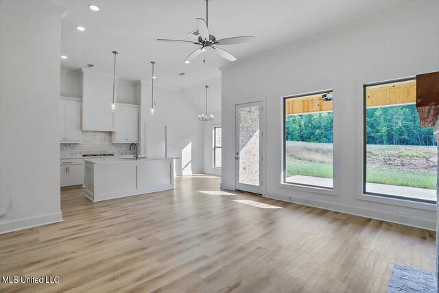 unfurnished living room with ceiling fan with notable chandelier, sink, a towering ceiling, and light wood-type flooring