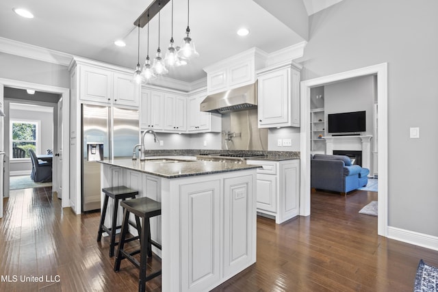 kitchen featuring a center island with sink, appliances with stainless steel finishes, white cabinetry, a sink, and ventilation hood