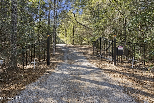 view of road featuring a gated entry, gravel driveway, a gate, and a view of trees