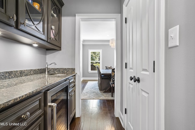 kitchen featuring wine cooler, dark wood-style flooring, a sink, dark stone counters, and glass insert cabinets