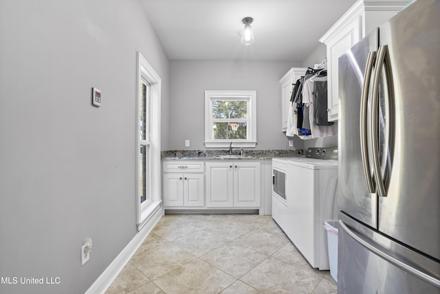 kitchen with washing machine and clothes dryer, stove, freestanding refrigerator, white cabinets, and a sink