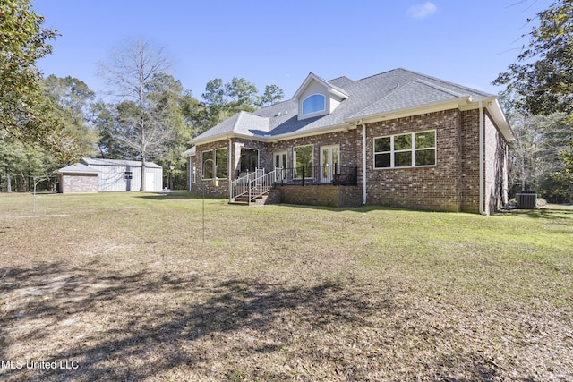 view of front of house with an outbuilding, brick siding, roof with shingles, a front yard, and central AC