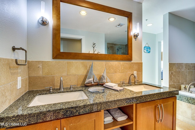 bathroom with double vanity, visible vents, tiled shower, and a sink