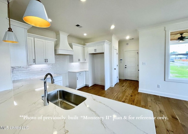 kitchen featuring sink, custom exhaust hood, light stone counters, pendant lighting, and white cabinets