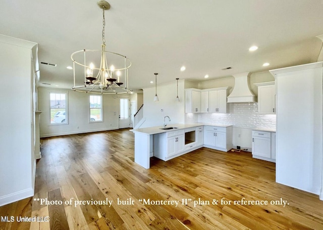 kitchen with sink, premium range hood, tasteful backsplash, white cabinets, and decorative light fixtures