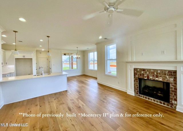 unfurnished living room with ceiling fan with notable chandelier, a tiled fireplace, sink, and light hardwood / wood-style flooring