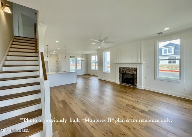 unfurnished living room with sink, a fireplace, ceiling fan with notable chandelier, and light hardwood / wood-style flooring