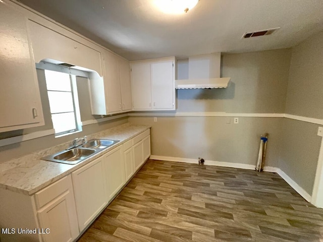 kitchen with visible vents, white cabinets, a sink, wood finished floors, and wall chimney exhaust hood